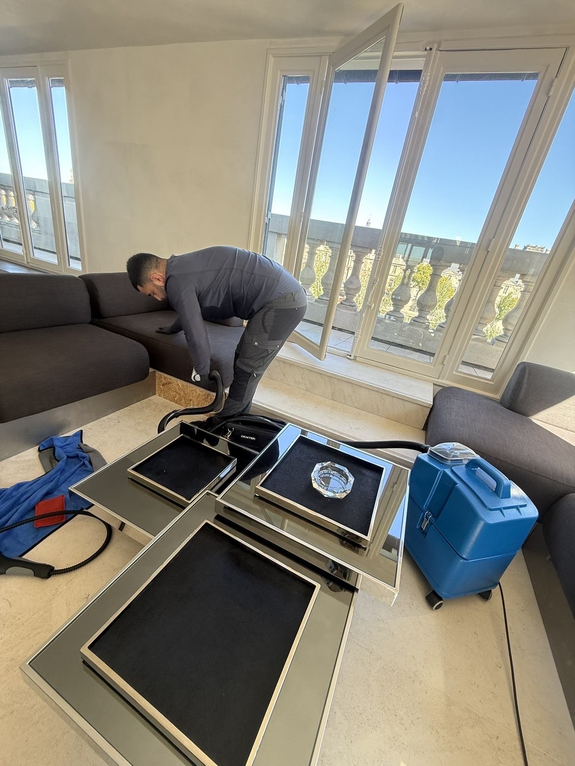 Wassil, fondateur de 2F Nettoyage, en pleine intervention de nettoyage professionnel d'un canapé dans un appartement avec vue à Paris